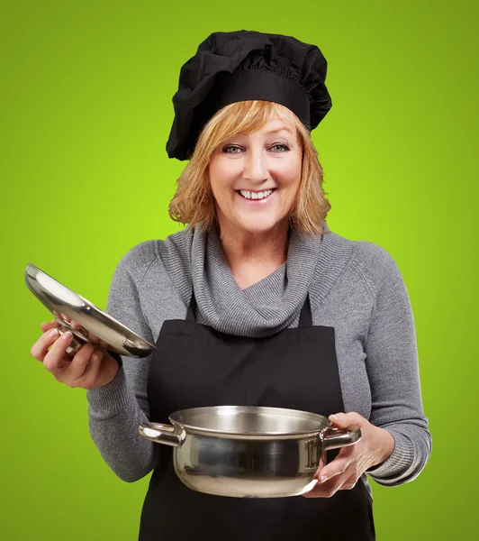 Μέσης ηλικίας γυναίκα μάγειρας που κρατά ένα τηγάνι souce πάνω από πράσινο φόντο — Φωτογραφία Αρχείου