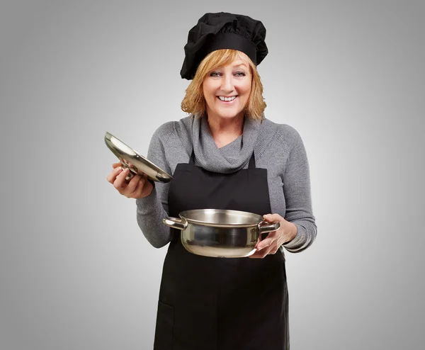 Μέσης ηλικίας γυναίκας μάγειρας κρατώντας ένα τηγάνι souce πέρα από το γκρι φόντο — Φωτογραφία Αρχείου