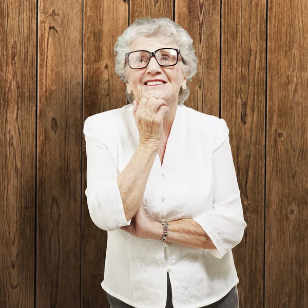 Portrait of senior woman thinking and looking up against a woode — Stock Photo, Image