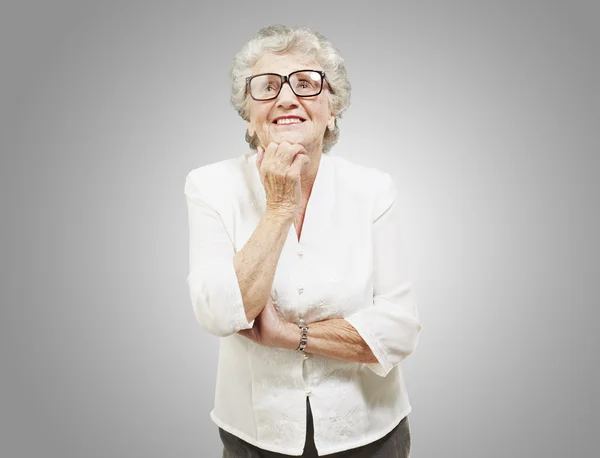 Retrato de mujer mayor pensando y mirando hacia arriba sobre respaldo gris — Foto de Stock