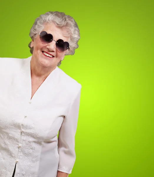 Retrato de mulher idosa feliz usando óculos de coração sobre verde — Fotografia de Stock