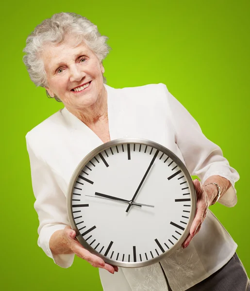 Portret szczęśliwą kobietą starszy gospodarstwa zegar na zielono — Zdjęcie stockowe