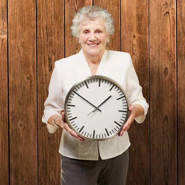 Porträt einer glücklichen Seniorin, die eine Uhr gegen eine hölzerne — Stockfoto