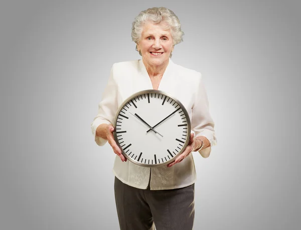 Bir kadın kıdemli mutlu holding saatin üzerine gri portresi — Stok fotoğraf