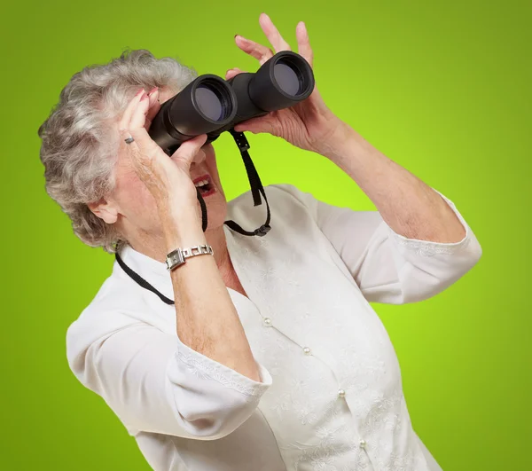 Retrato de una mujer mayor mirando a través de unos prismáticos sobre verde — Foto de Stock