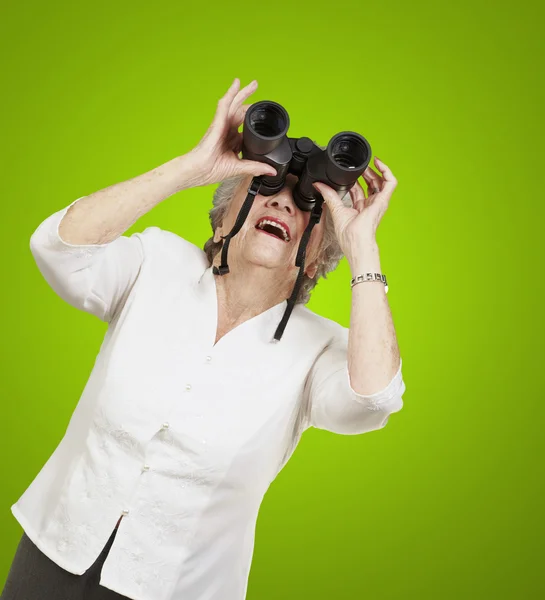 Retrato de mulher idosa olhando através de um binóculos contra um — Fotografia de Stock