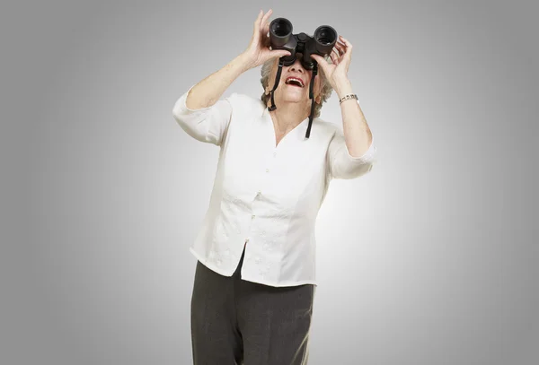 Retrato de mulher idosa olhando através de um binóculos contra um — Fotografia de Stock