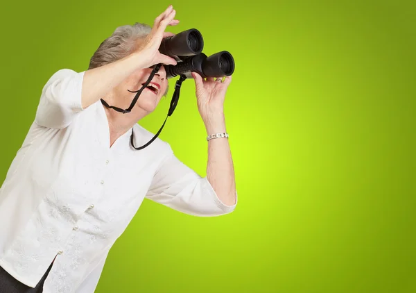 Retrato de una mujer mayor mirando a través de unos prismáticos sobre verde —  Fotos de Stock