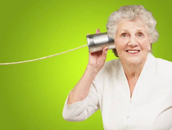 Portrait de femme âgée entendant avec boîte de conserve en métal sur vert b — Photo