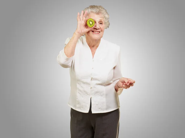 Retrato de mujer mayor sosteniendo kiwi delante de su ojo sobre g —  Fotos de Stock