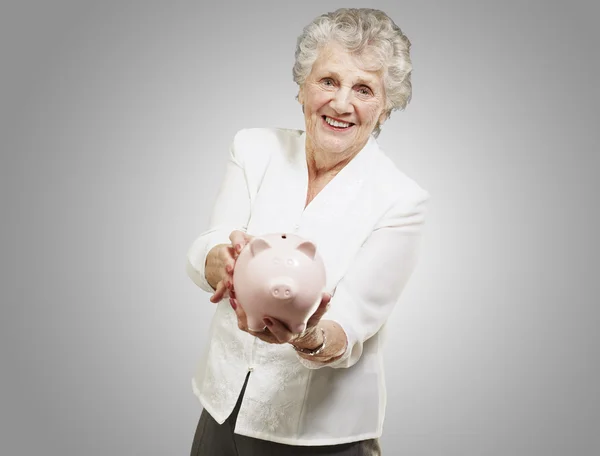 Retrato de mulher sênior mostrando um banco porquinho sobre backgrou cinza — Fotografia de Stock