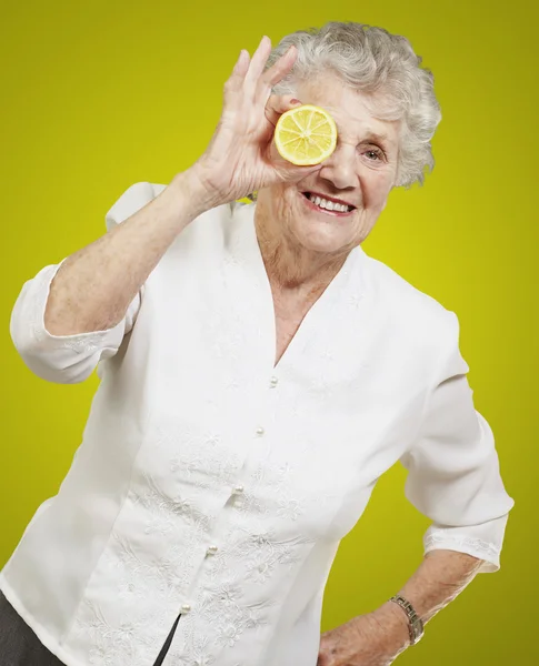 Portrait of senior woman with lemon in front of her eye over yel — Stock Photo, Image