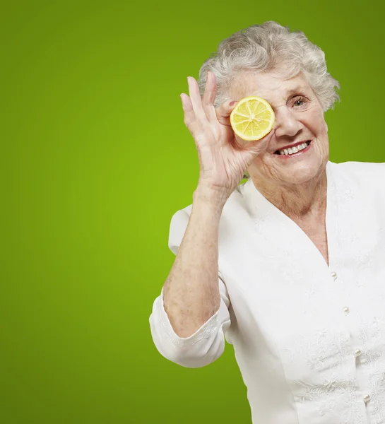 Portrait of senior woman with lemon in front of her eye over gre — Stock Photo, Image