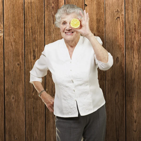 Portrét starší ženy s citronem před její oko proti — Stock fotografie