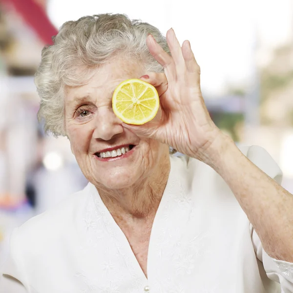 Portrait of senior woman with lemon in front of her eye against — Stock Photo, Image