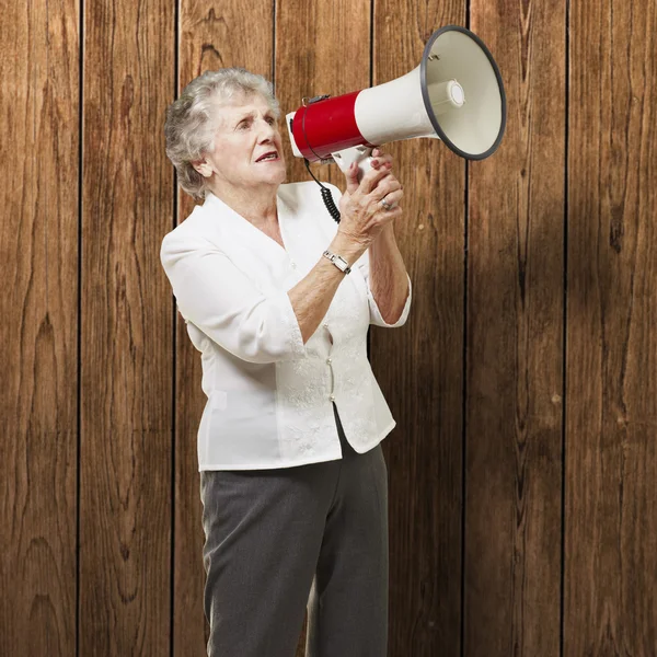 Portrait of senior woman holding megaphone over wooden wall — Stock Photo, Image