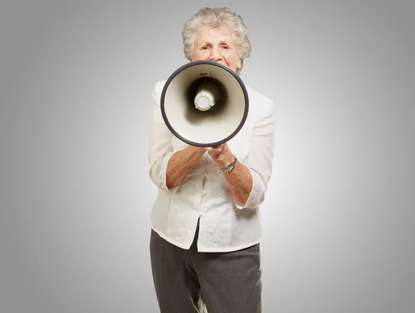 Портрет пожилой женщины, кричащей с мегафоном над серой спиной — стоковое фото