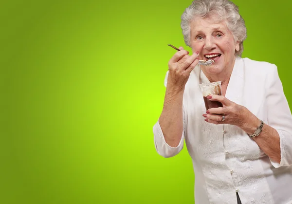 Portrait of senior woman eating chocolate and cream cup over gre — Stock Photo, Image