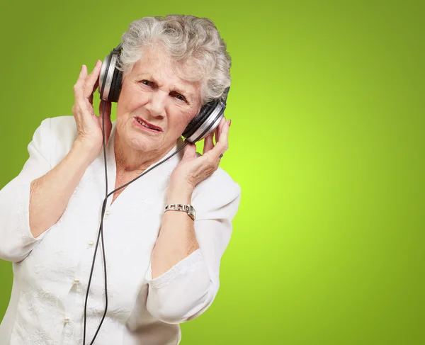 Porträt einer Seniorin, die vor grünem Hintergrund Musik hört — Stockfoto