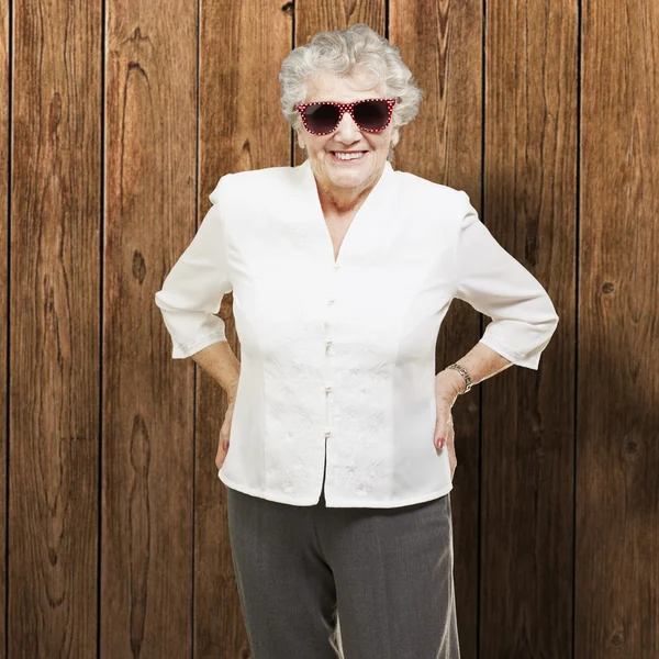 Retrato de mulher idosa de pé usando óculos de sol contra um w — Fotografia de Stock