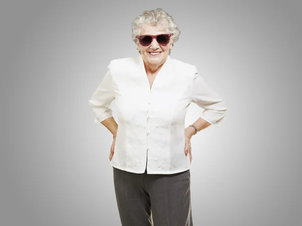 Portrait of senior woman standing wearing sunglasses over grey b — Stock Photo, Image