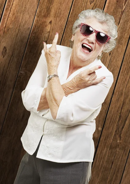 Portrét starší ženy dělají rock symbolem dřevěné zdi — Stock fotografie