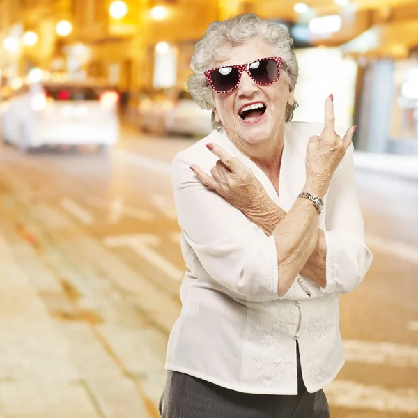 Portrait d'une femme âgée faisant du rock symbole contre une nuit en ville — Photo