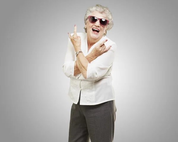 Porträtt av äldre kvinna gör rock symbol över grå bakgrund — Stockfoto