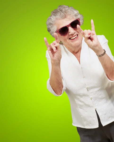Портрет счастливой пожилой женщины, изображающей рок-символ над зеленой бабой — стоковое фото