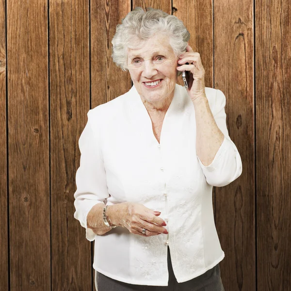 Portret van senior vrouw praten op mobiele telefoon tegen een houten muur — Stockfoto