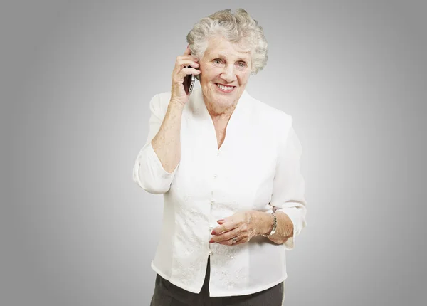 Портрет пожилой женщины, разговаривающей по мобильному телефону на сером фоне — стоковое фото