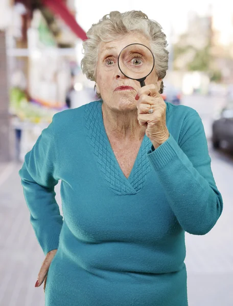 Portrait of senior woman looking through a magnifying glass agai — Stock Photo, Image