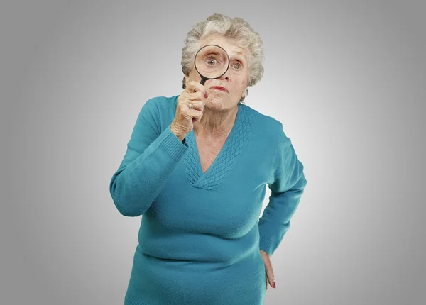 Портрет пожилой женщины, смотрящей через увеличительное стекло — стоковое фото