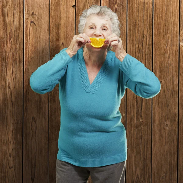 Retrato de mulher idosa segurando uma fatia de laranja na frente dela — Fotografia de Stock