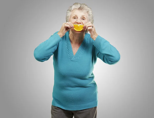 Retrato de una mujer mayor sosteniendo una rebanada de naranja frente a ella — Foto de Stock