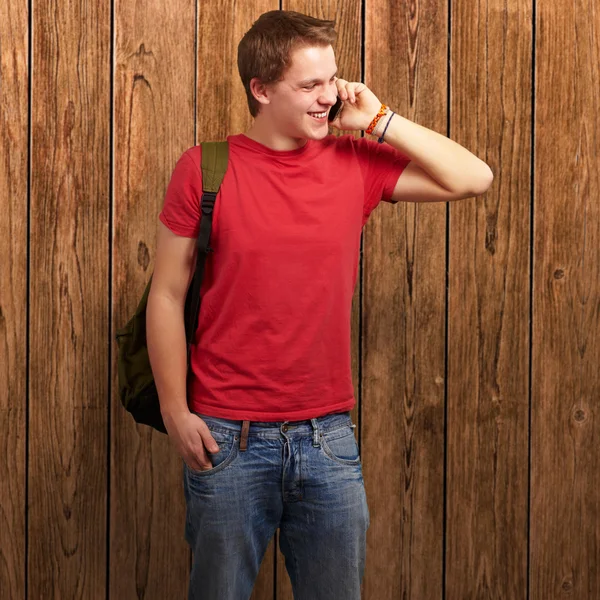 Portret młodzieńca rozmowy na telefon komórkowy o ścianę drewniane — Zdjęcie stockowe