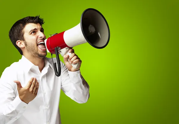 Portrait of young man shouting with megaphone over green backgro — Stock Photo, Image