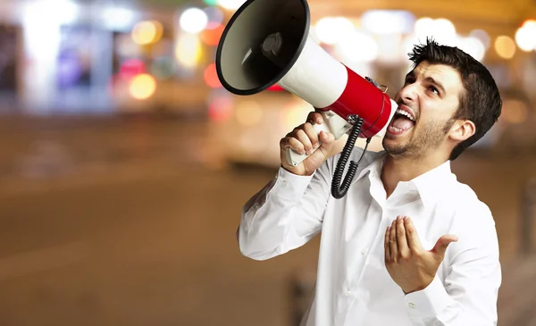 Portrait of young man shouting with megaphone at city by night — Stock Photo, Image