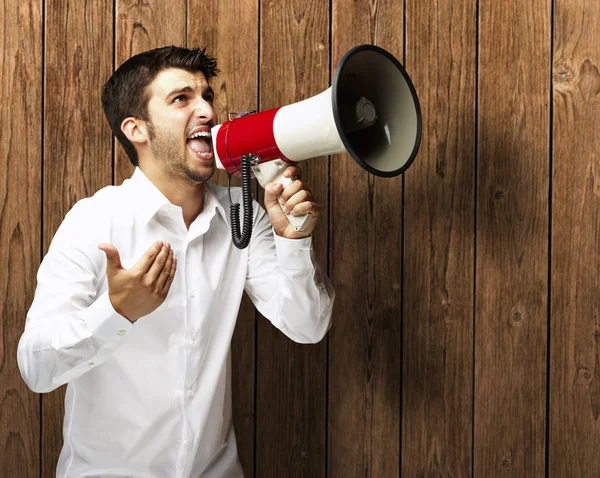 Portret van jonge man schreeuwen met megafoon tegen een houten w — Stockfoto