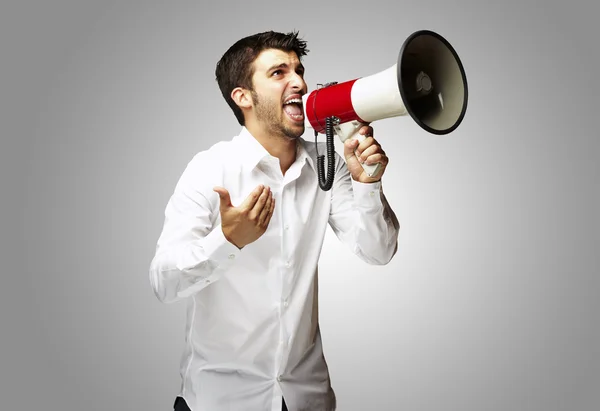 Portrét mladého muže s megafon křičet nad šedou poz — Stock fotografie