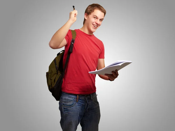 Retrato de estudiante guapo sosteniendo cuaderno y pluma sobre gris —  Fotos de Stock