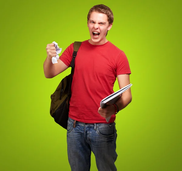 Giovane studente arrabbiato uomo sgrossatura un foglio su sfondo verde — Foto Stock