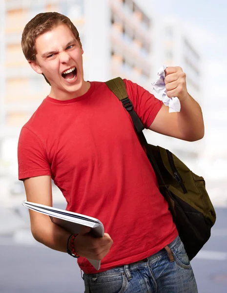 Joven estudiante enojado golpeando una hoja contra una universidad — Foto de Stock