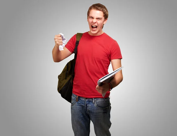 Jonge boos student man Afbramen van een blad over grijze achtergrond — Stockfoto