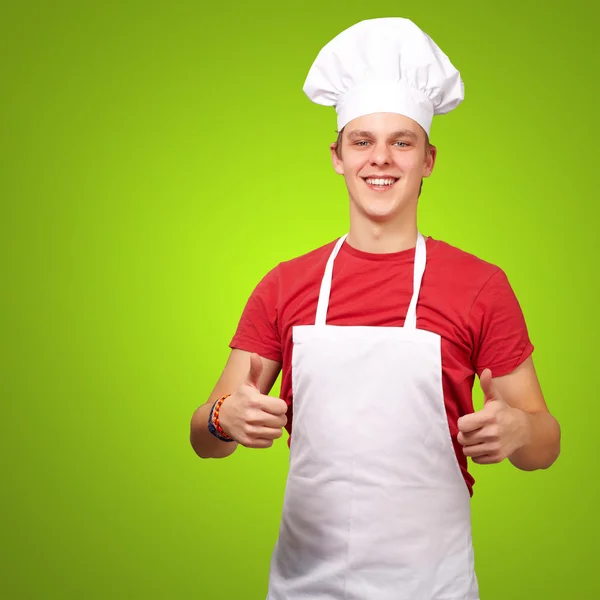 Портрет молодого кухаря, який робить символ успіху над зеленим фоном — стокове фото