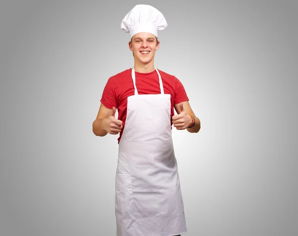 Porträt eines jungen Kochs, der Erfolgssymbol über grauem Backgr macht — Stockfoto