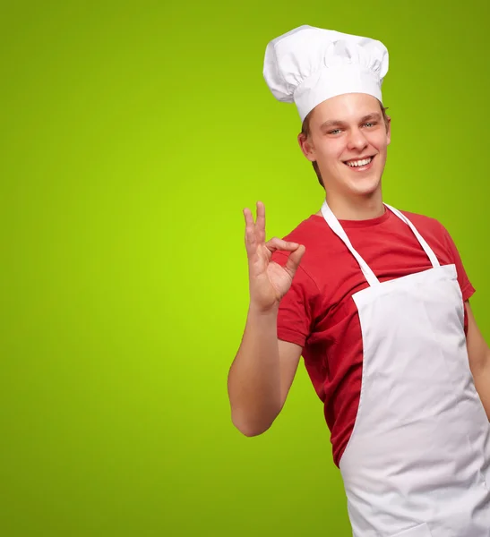 Retrato del joven cocinero haciendo símbolo de éxito sobre el respaldo verde — Foto de Stock