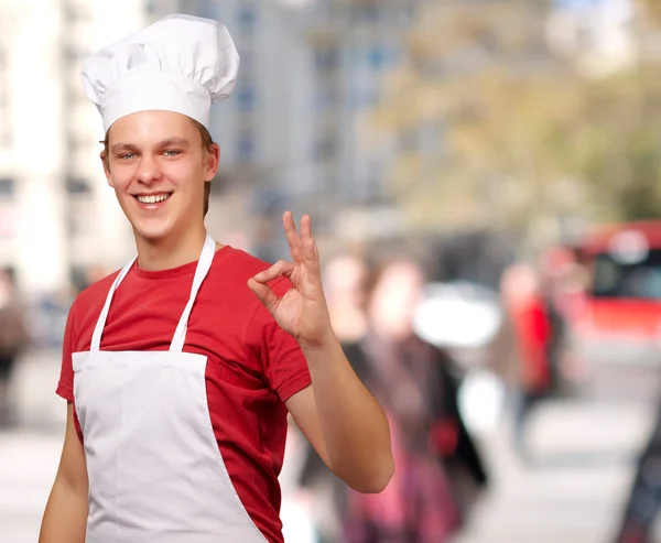 Retrato de jovem cozinheiro fazendo símbolo de sucesso em stree lotado — Fotografia de Stock