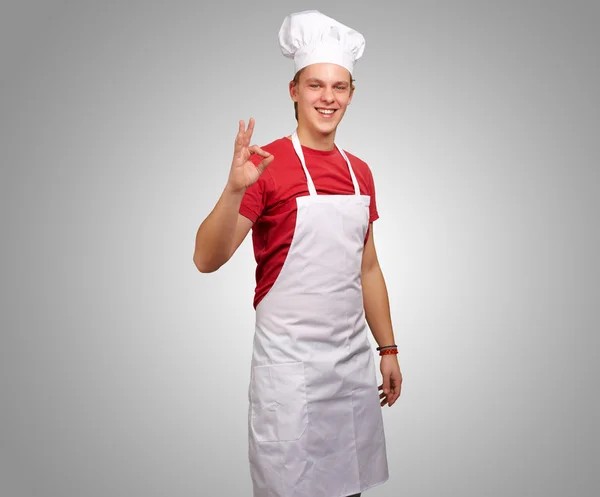Portrét mladého kuchaře člověka dělá symbolem úspěchu proti šedé b — Stock fotografie
