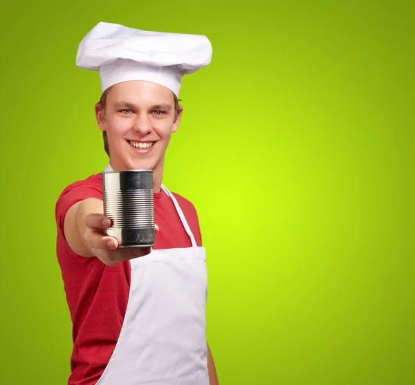 Portrait of young cook man holding a metal tin can over green ba — Stock Photo, Image